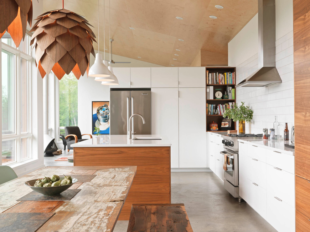 Bild på ett funkis kök, med en undermonterad diskho, släta luckor, vita skåp, vitt stänkskydd, stänkskydd i tunnelbanekakel, rostfria vitvaror, betonggolv, en köksö och grått golv