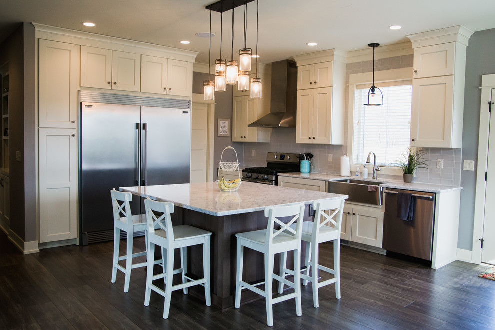 Arts and crafts l-shaped laminate floor and brown floor eat-in kitchen photo in Grand Rapids with a farmhouse sink, shaker cabinets, white cabinets, quartz countertops, gray backsplash, ceramic backsplash, stainless steel appliances, an island and white countertops