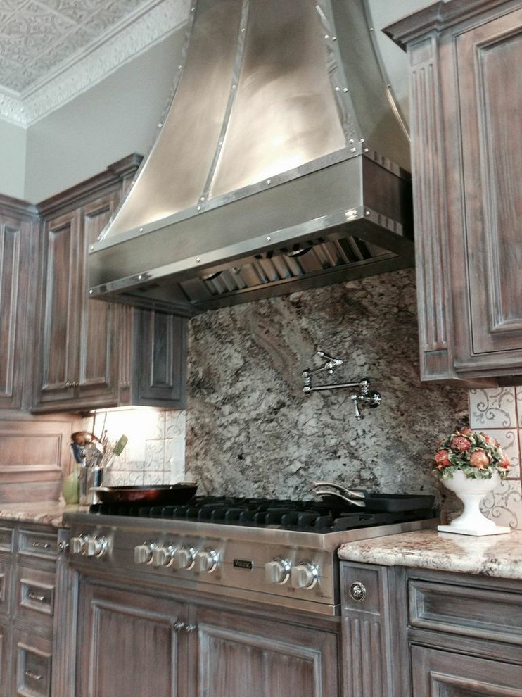 Photo of a large rustic l-shaped kitchen pantry in San Francisco with recessed-panel cabinets, distressed cabinets, granite worktops, multi-coloured splashback, stainless steel appliances and an island.