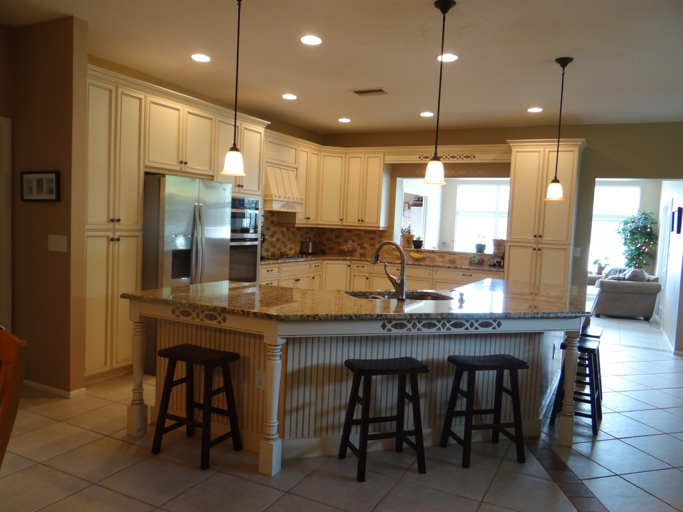 Klassisk inredning av ett stort kök, med en undermonterad diskho, släta luckor, vita skåp, granitbänkskiva, flerfärgad stänkskydd, rostfria vitvaror, klinkergolv i keramik och en köksö