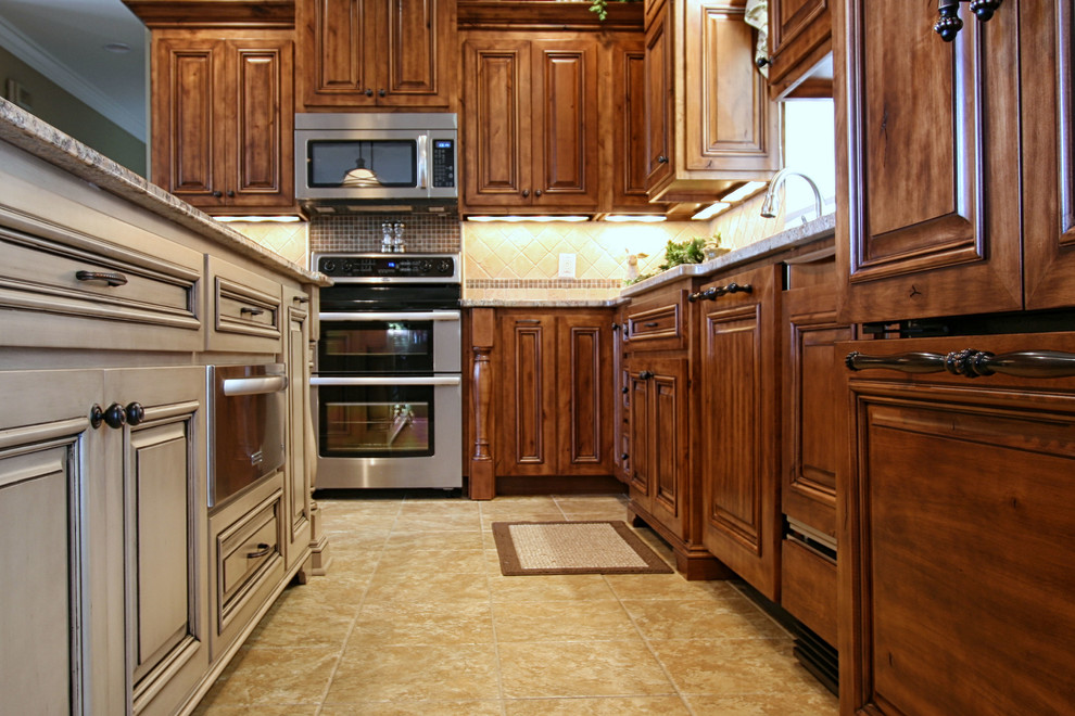 Cette photo montre une cuisine américaine chic en L avec un évier intégré, un placard avec porte à panneau surélevé, des portes de placard marrons, un plan de travail en granite et une crédence beige.