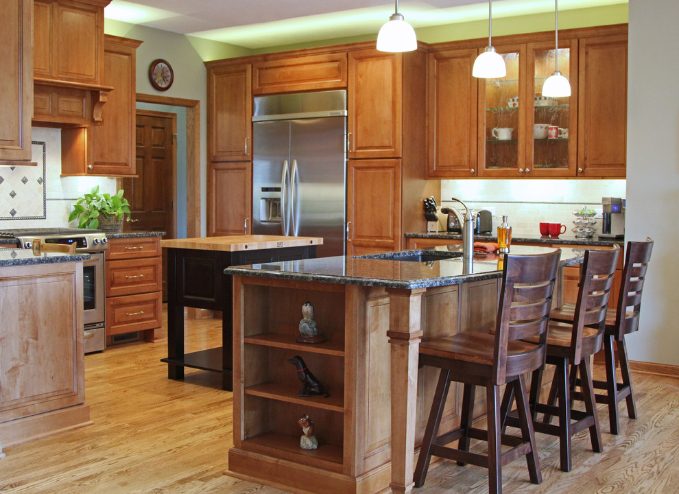 Bild på ett mellanstort vintage svart svart kök, med en undermonterad diskho, luckor med upphöjd panel, skåp i mellenmörkt trä, granitbänkskiva, beige stänkskydd, stänkskydd i travertin, rostfria vitvaror, mellanmörkt trägolv, flera köksöar och brunt golv