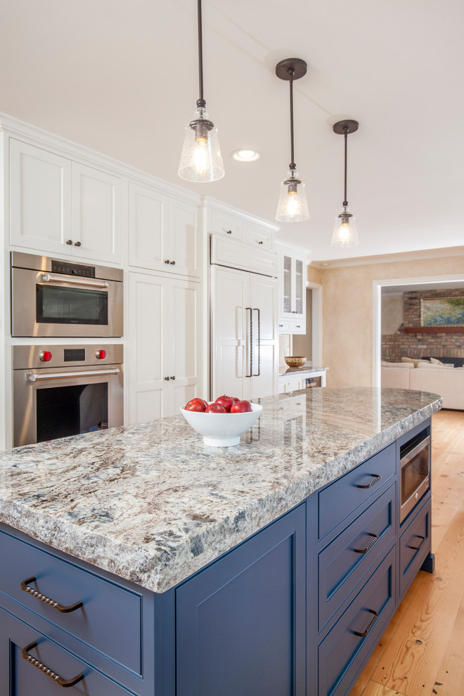 Inspiration for a mid-sized transitional l-shaped medium tone wood floor and brown floor kitchen remodel in Minneapolis with a farmhouse sink, shaker cabinets, white cabinets, granite countertops, white backsplash, subway tile backsplash, stainless steel appliances and an island