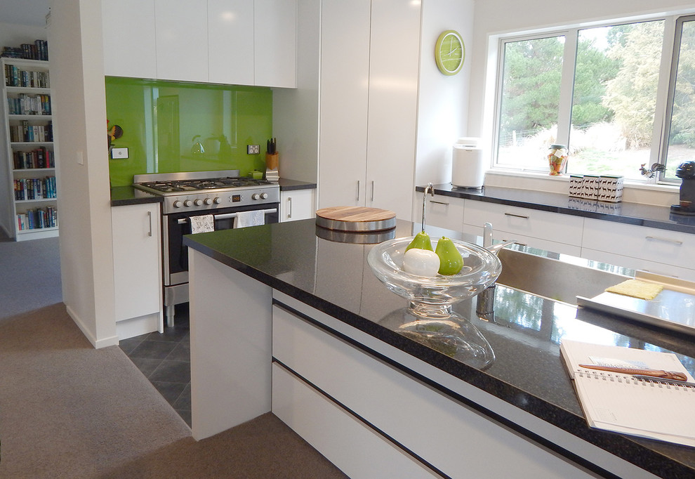 Photo of a medium sized contemporary l-shaped open plan kitchen in Christchurch with a built-in sink, flat-panel cabinets, white cabinets, laminate countertops, green splashback, glass sheet splashback, stainless steel appliances, vinyl flooring and an island.