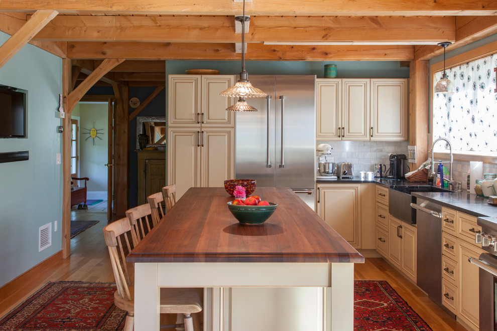 Idéer för att renovera ett mellanstort lantligt kök, med en rustik diskho, luckor med upphöjd panel, gula skåp, bänkskiva i täljsten, grått stänkskydd, stänkskydd i stenkakel, rostfria vitvaror, mellanmörkt trägolv och en köksö