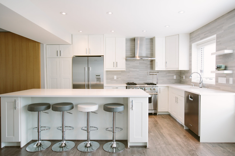 Moderne Küche in L-Form mit Unterbauwaschbecken, Schrankfronten im Shaker-Stil, weißen Schränken, Küchenrückwand in Grau und Küchengeräten aus Edelstahl in Calgary