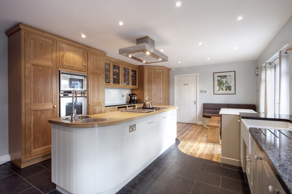 This is an example of a traditional kitchen in London with stainless steel appliances, a belfast sink, granite worktops, recessed-panel cabinets, light wood cabinets and an island.