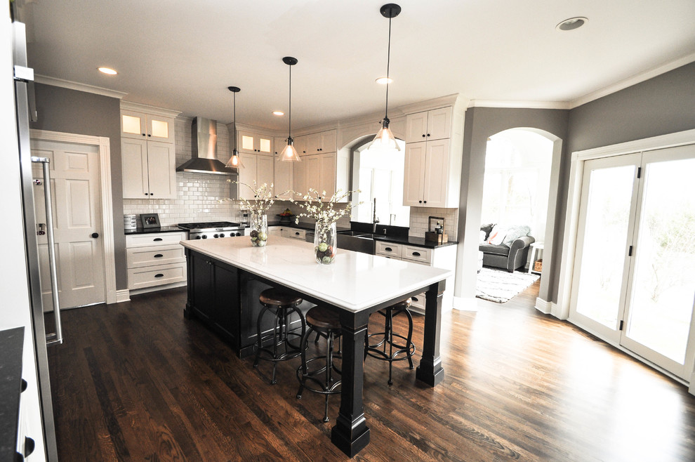 Example of a large farmhouse u-shaped medium tone wood floor and brown floor eat-in kitchen design in Minneapolis with shaker cabinets, white cabinets, quartz countertops, subway tile backsplash, stainless steel appliances, an island, a farmhouse sink and white backsplash