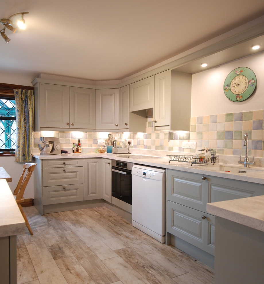 Large cottage u-shaped porcelain tile and brown floor eat-in kitchen photo in Surrey with an undermount sink, raised-panel cabinets, blue cabinets, solid surface countertops, white backsplash, ceramic backsplash, an island and white countertops