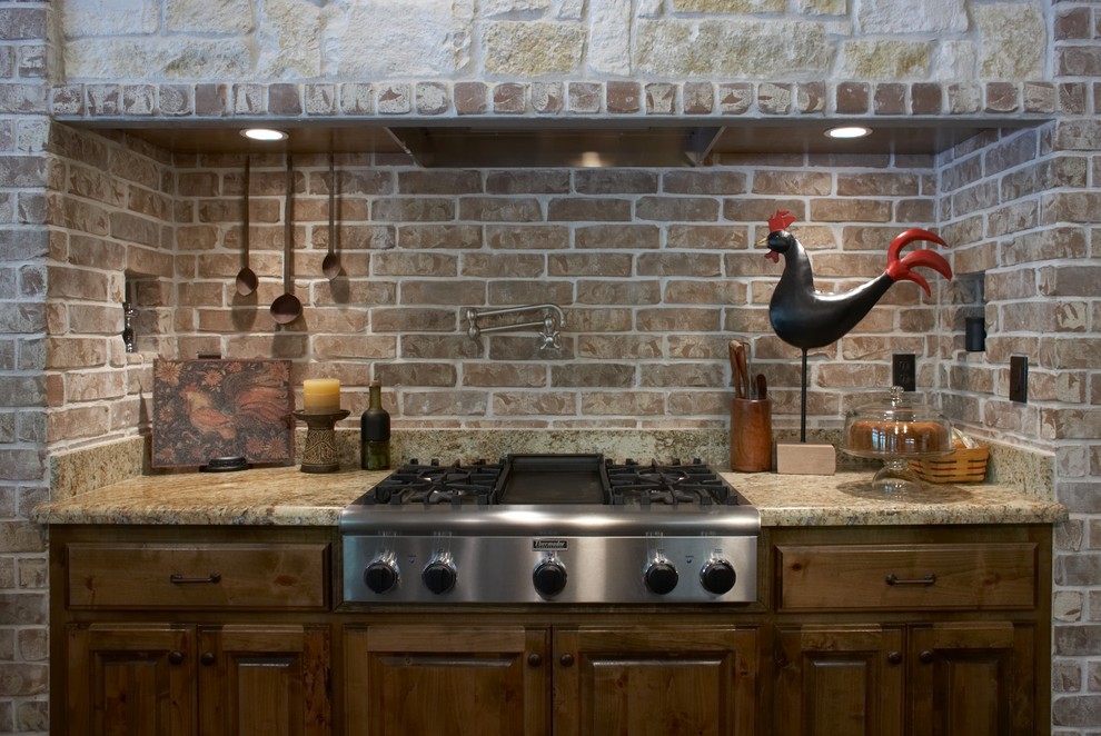 Lantlig inredning av ett avskilt, mellanstort u-kök, med en rustik diskho, luckor med upphöjd panel, skåp i mellenmörkt trä, granitbänkskiva, rött stänkskydd, stänkskydd i tunnelbanekakel, rostfria vitvaror och en köksö