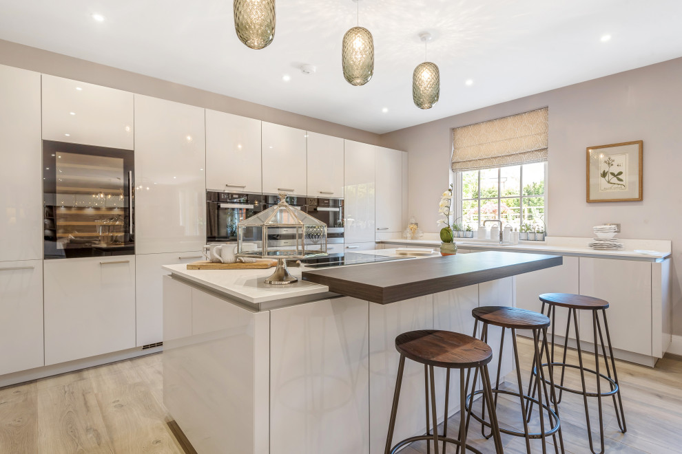 Immagine di una cucina minimal con ante lisce, ante bianche, elettrodomestici in acciaio inossidabile, parquet chiaro, pavimento beige e top bianco