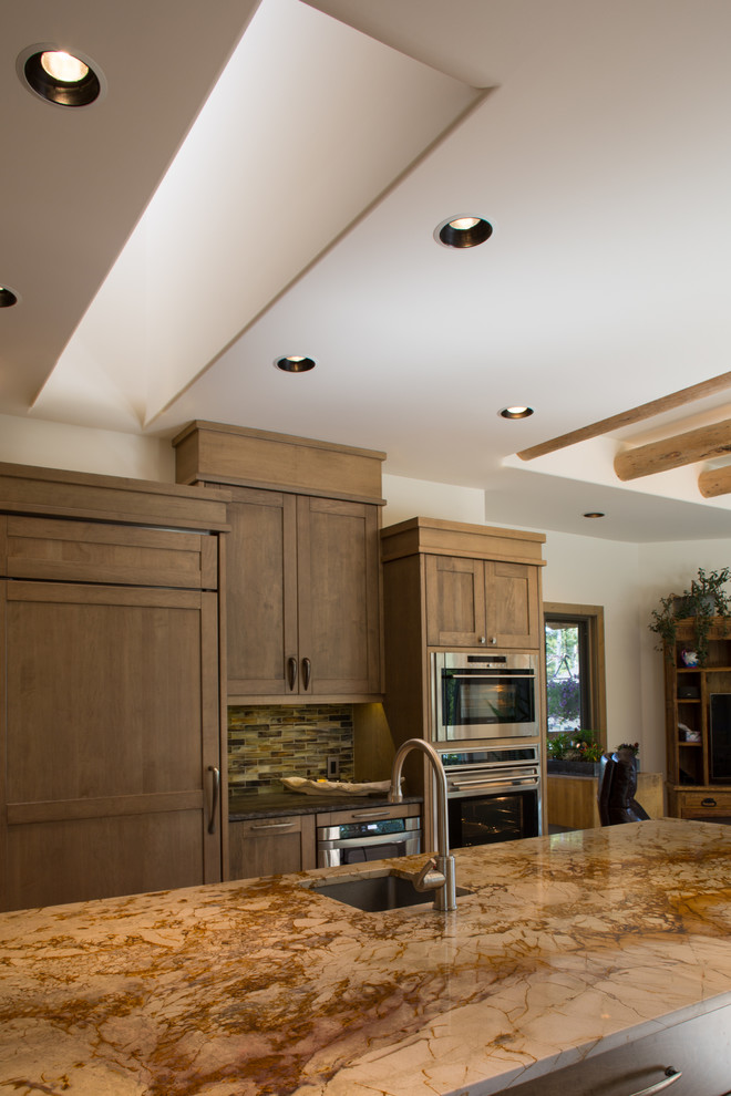 Example of a large mountain style u-shaped light wood floor open concept kitchen design in Calgary with a single-bowl sink, shaker cabinets, medium tone wood cabinets, granite countertops, multicolored backsplash, matchstick tile backsplash, paneled appliances and an island