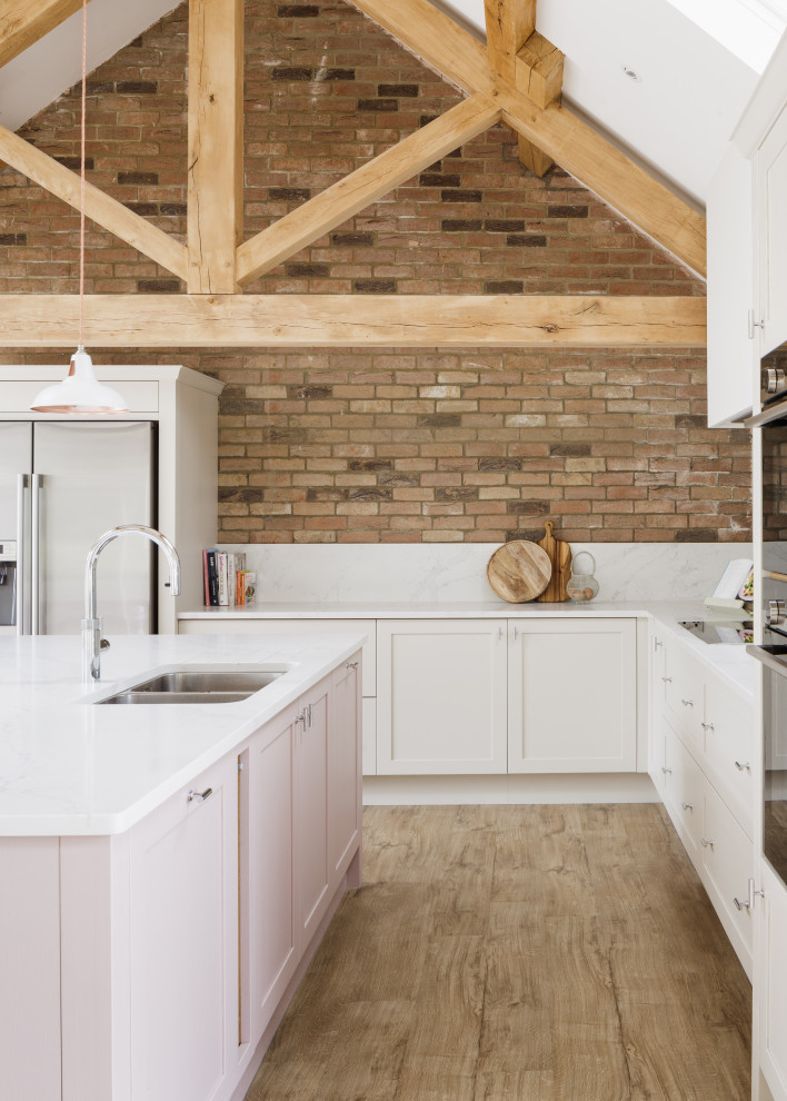 Photo of a medium sized farmhouse u-shaped open plan kitchen in Other with a double-bowl sink, shaker cabinets, pink cabinets, composite countertops, white splashback, engineered quartz splashback, stainless steel appliances, light hardwood flooring, an island, brown floors, white worktops and a vaulted ceiling.