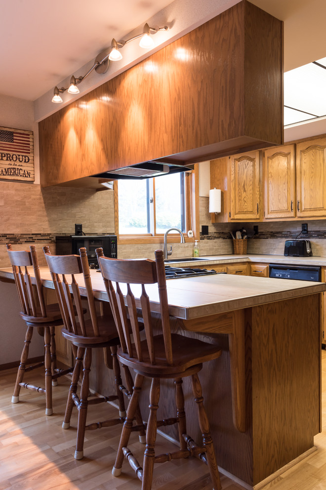 Immagine di una cucina con lavello a doppia vasca, ante con bugna sagomata, ante in legno scuro, top piastrellato, paraspruzzi beige e elettrodomestici neri