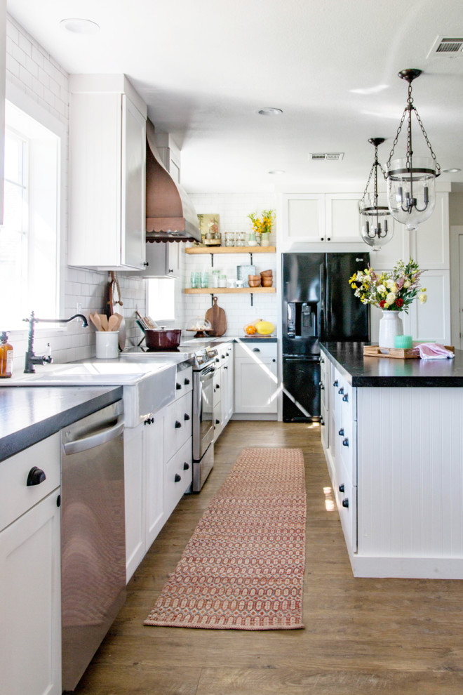 Foto på ett lantligt kök, med en rustik diskho, skåp i shakerstil, vita skåp, bänkskiva i onyx, vitt stänkskydd, stänkskydd i tunnelbanekakel, svarta vitvaror, mellanmörkt trägolv, en köksö och brunt golv