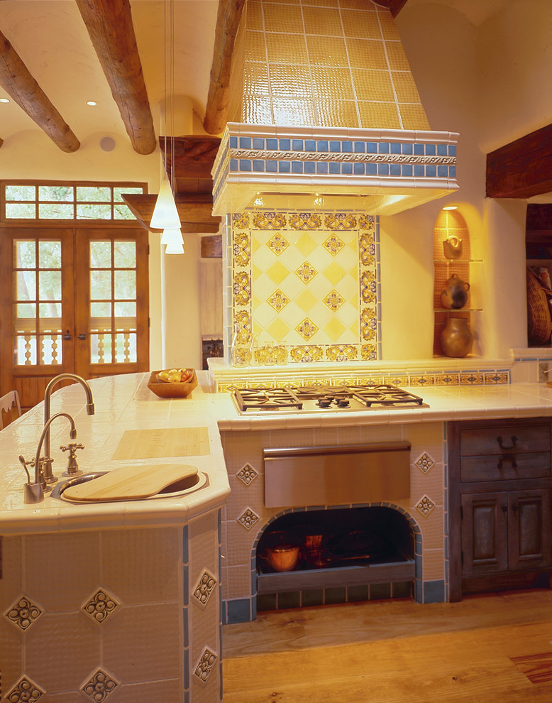 Eat-in kitchen - mid-sized mediterranean l-shaped light wood floor eat-in kitchen idea in Albuquerque with a drop-in sink, recessed-panel cabinets, distressed cabinets, tile countertops, multicolored backsplash, ceramic backsplash and stainless steel appliances