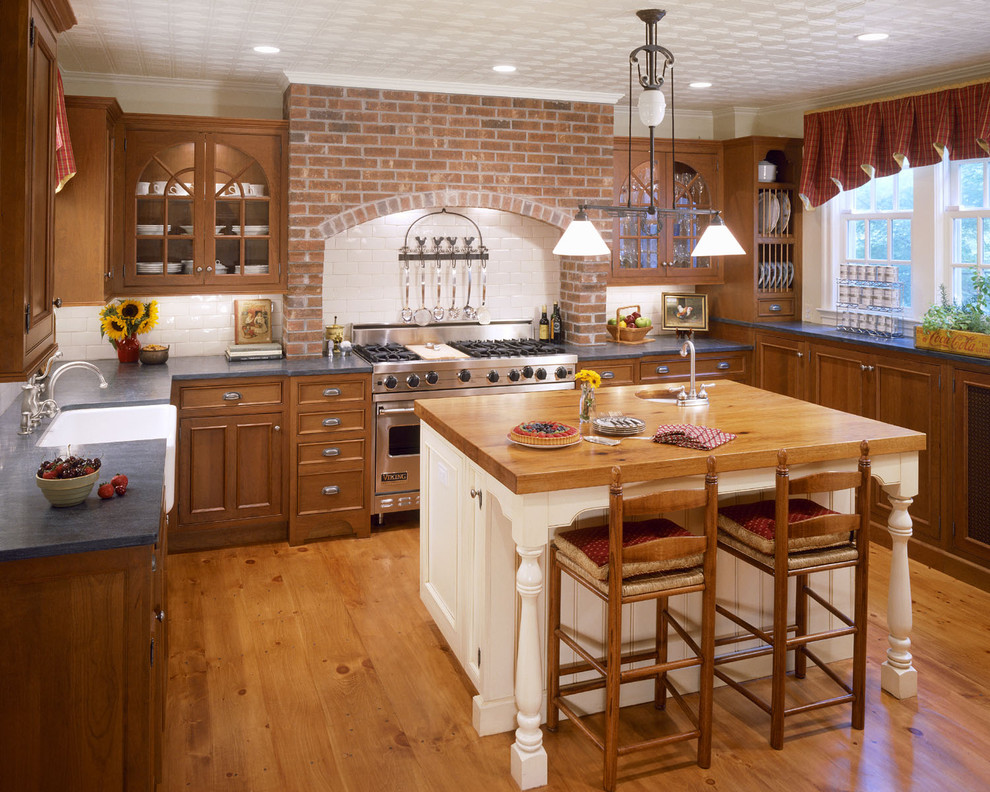 Inredning av ett klassiskt mellanstort kök, med luckor med profilerade fronter, en rustik diskho, granitbänkskiva, skåp i mellenmörkt trä, vitt stänkskydd, stänkskydd i tunnelbanekakel, rostfria vitvaror, mellanmörkt trägolv och en köksö