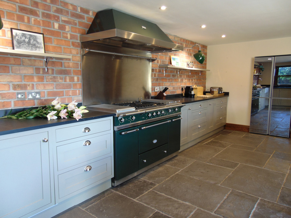Medium sized traditional l-shaped kitchen/diner with a belfast sink, shaker cabinets, grey cabinets, coloured appliances, limestone flooring, no island, grey floors and black worktops.