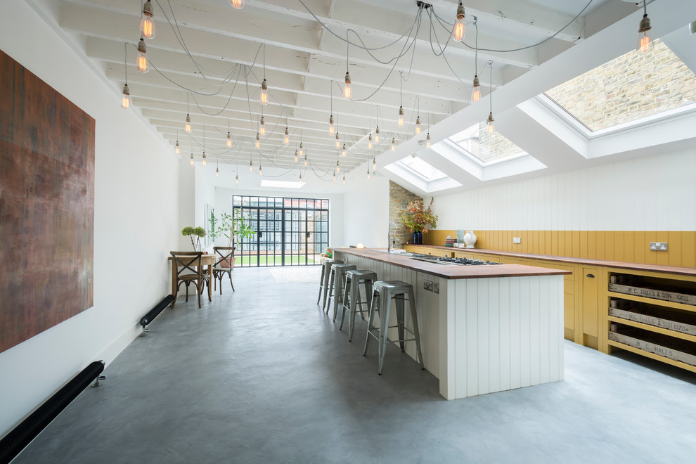 Photo of a large rural galley open plan kitchen in London with wood worktops, concrete flooring, an island, flat-panel cabinets and yellow cabinets.