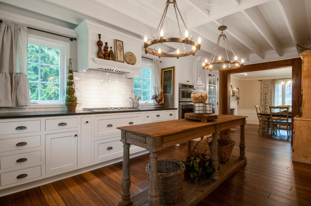 Cottage u-shaped medium tone wood floor and brown floor eat-in kitchen photo in Seattle with a farmhouse sink, shaker cabinets, white cabinets, quartz countertops, white backsplash, subway tile backsplash, stainless steel appliances and an island