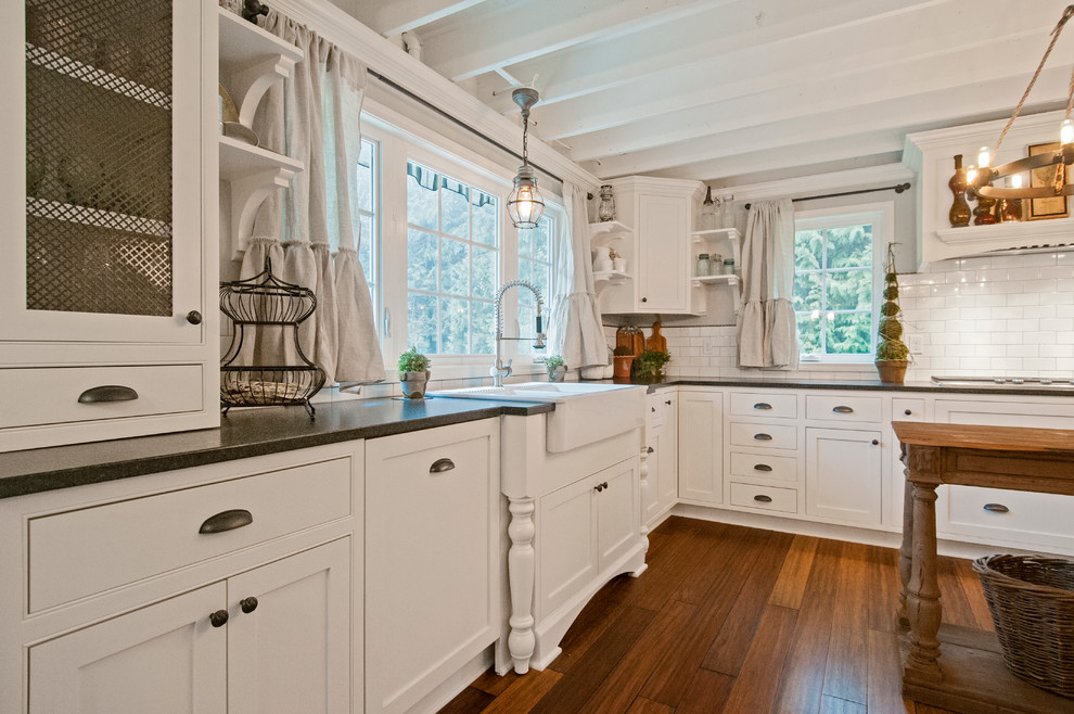 Foto på ett lantligt kök, med en rustik diskho, skåp i shakerstil, vita skåp, bänkskiva i kvarts, vitt stänkskydd, stänkskydd i tunnelbanekakel, rostfria vitvaror, mellanmörkt trägolv, en köksö och brunt golv