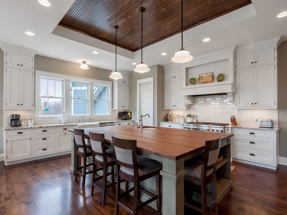 Example of a large country u-shaped medium tone wood floor and brown floor open concept kitchen design in Minneapolis with flat-panel cabinets, white cabinets, marble countertops, beige backsplash, subway tile backsplash, stainless steel appliances, an island and brown countertops