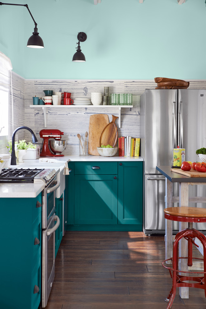 Cette photo montre une petite cuisine bord de mer en L avec un évier de ferme, un placard à porte shaker, des portes de placard turquoises, un plan de travail en quartz modifié, une crédence grise, une crédence en carreau de porcelaine, un électroménager en acier inoxydable, îlot, un sol marron, un plan de travail blanc et un sol en bois brun.