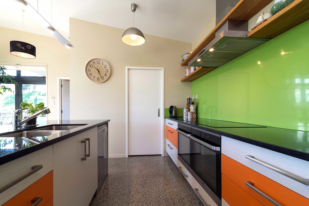 Inspiration för moderna parallellkök, med orange skåp, granitbänkskiva, grönt stänkskydd, rostfria vitvaror, betonggolv och en köksö