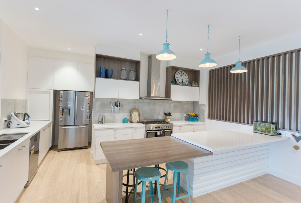 This is an example of a large contemporary u-shaped kitchen/diner in Melbourne with a submerged sink, grey splashback, stainless steel appliances, bamboo flooring, an island, flat-panel cabinets, white cabinets, engineered stone countertops, stone tiled splashback, beige floors and white worktops.