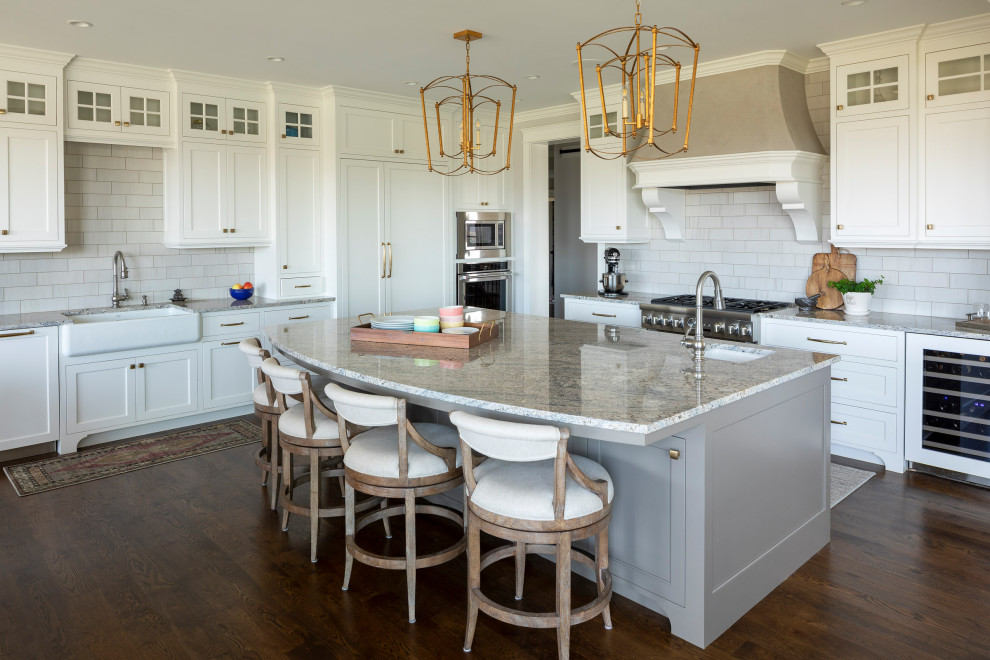 Photo of a large traditional l-shaped kitchen in Minneapolis with a belfast sink, shaker cabinets, white cabinets, grey splashback, ceramic splashback, stainless steel appliances, medium hardwood flooring, an island, brown floors and grey worktops.