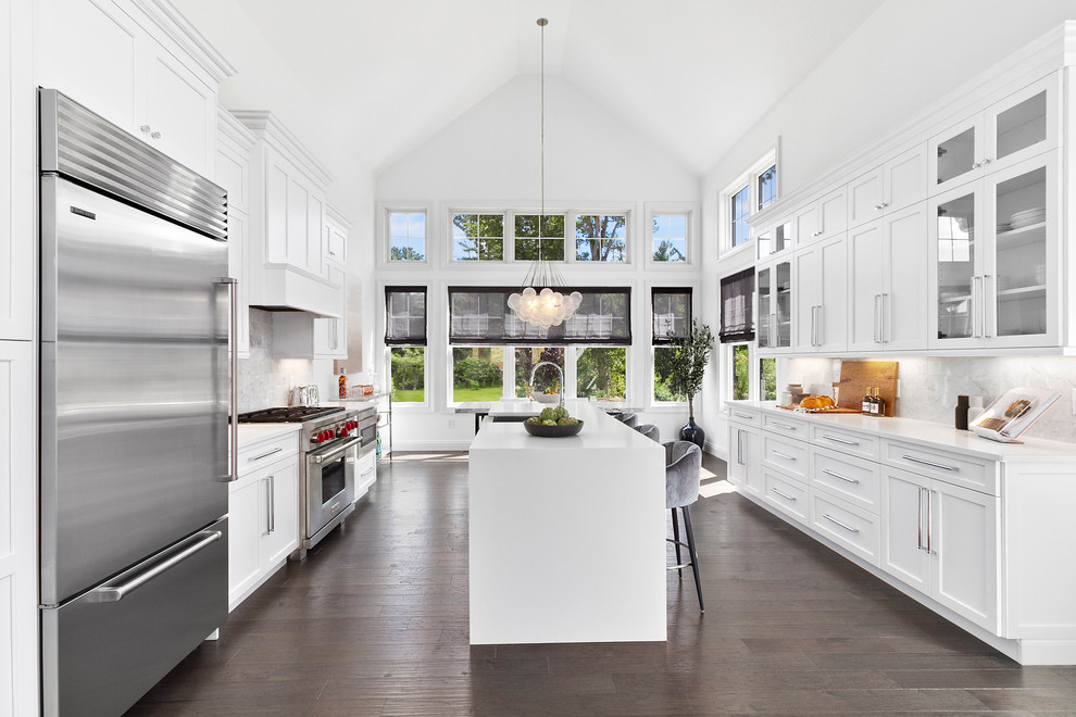 Transitional galley brown floor and dark wood floor kitchen photo in New York with shaker cabinets, white cabinets, quartzite countertops, gray backsplash, marble backsplash, stainless steel appliances, an island, white countertops and a farmhouse sink