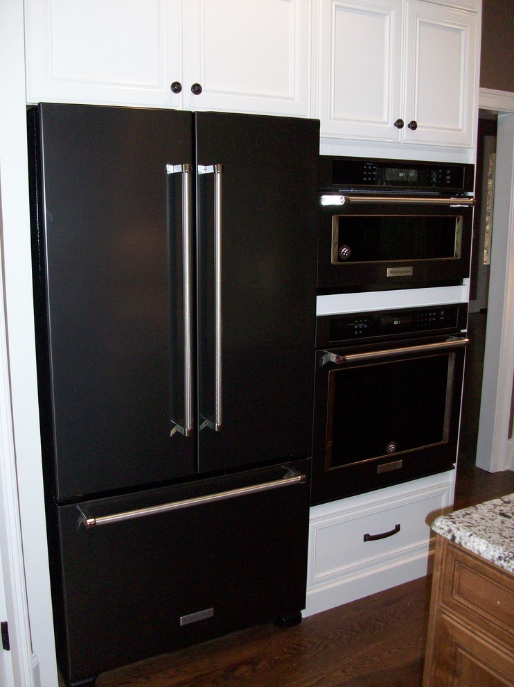 Bild på ett avskilt, mellanstort u-kök, med luckor med infälld panel, vita skåp, granitbänkskiva, stänkskydd i tegel, svarta vitvaror, mörkt trägolv, en köksö och en rustik diskho