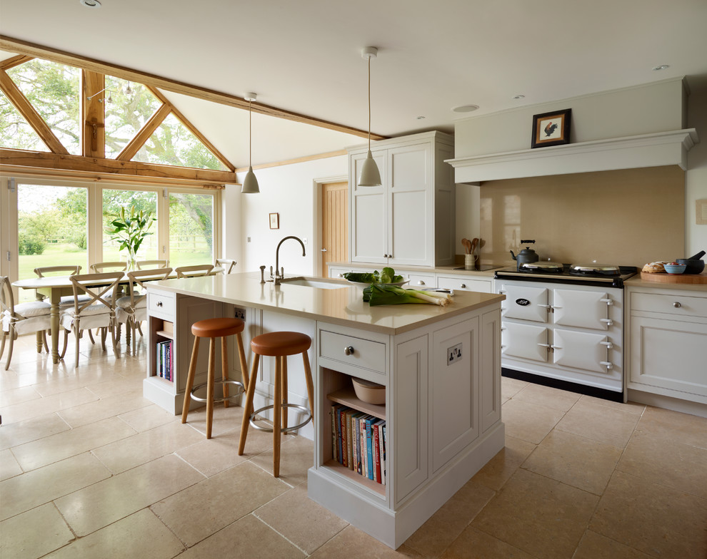 Idée de décoration pour une cuisine américaine champêtre avec un évier encastré, un placard avec porte à panneau encastré, des portes de placard blanches, une crédence beige et îlot.