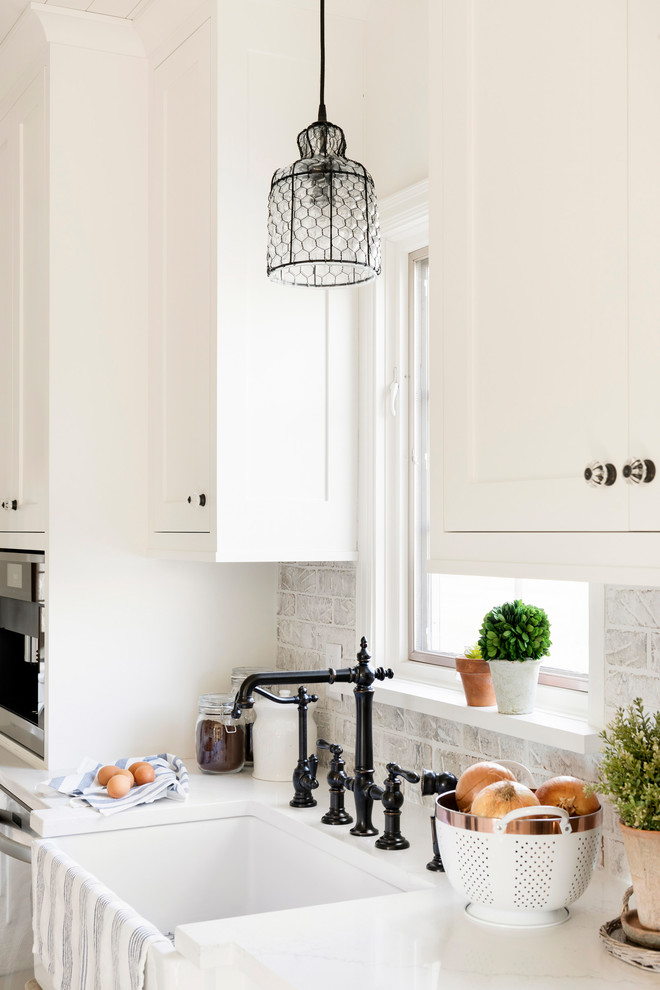 Inspiration for a country u-shaped kitchen/diner in Minneapolis with a belfast sink, white cabinets, white splashback, brick splashback, stainless steel appliances, light hardwood flooring, an island, beige floors and white worktops.