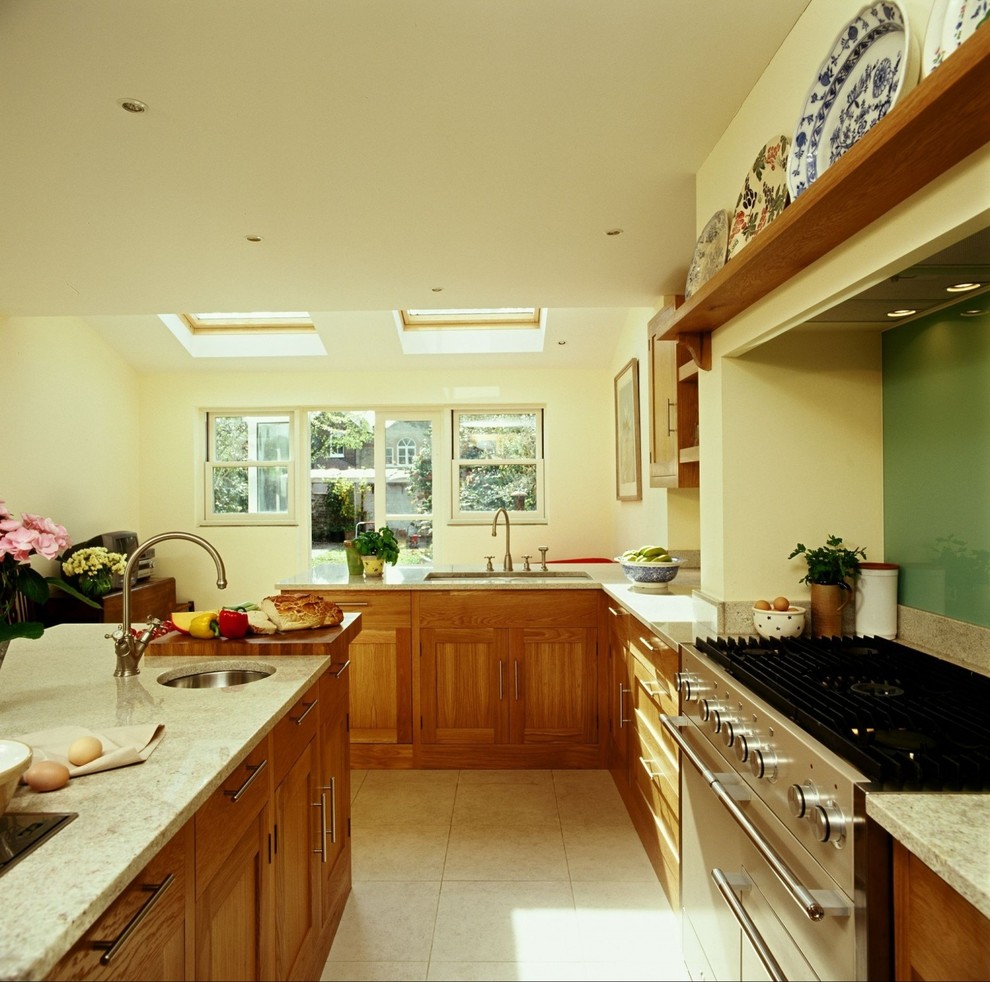 Große Landhausstil Wohnküche in L-Form mit Einbauwaschbecken, Schrankfronten im Shaker-Stil, hellbraunen Holzschränken, Granit-Arbeitsplatte, Küchenrückwand in Grün, Glasrückwand, Küchengeräten aus Edelstahl und Kücheninsel in Surrey