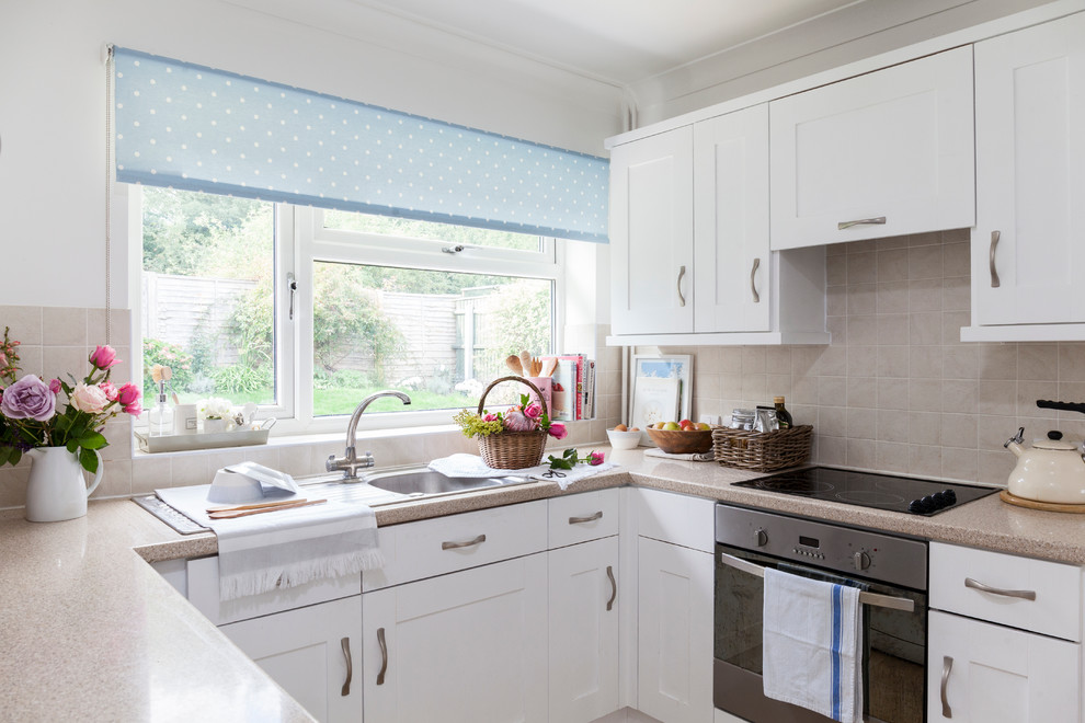 Photo of a small farmhouse u-shaped enclosed kitchen in London with a single-bowl sink, recessed-panel cabinets, white cabinets, laminate countertops, beige splashback, ceramic splashback, stainless steel appliances, lino flooring and no island.
