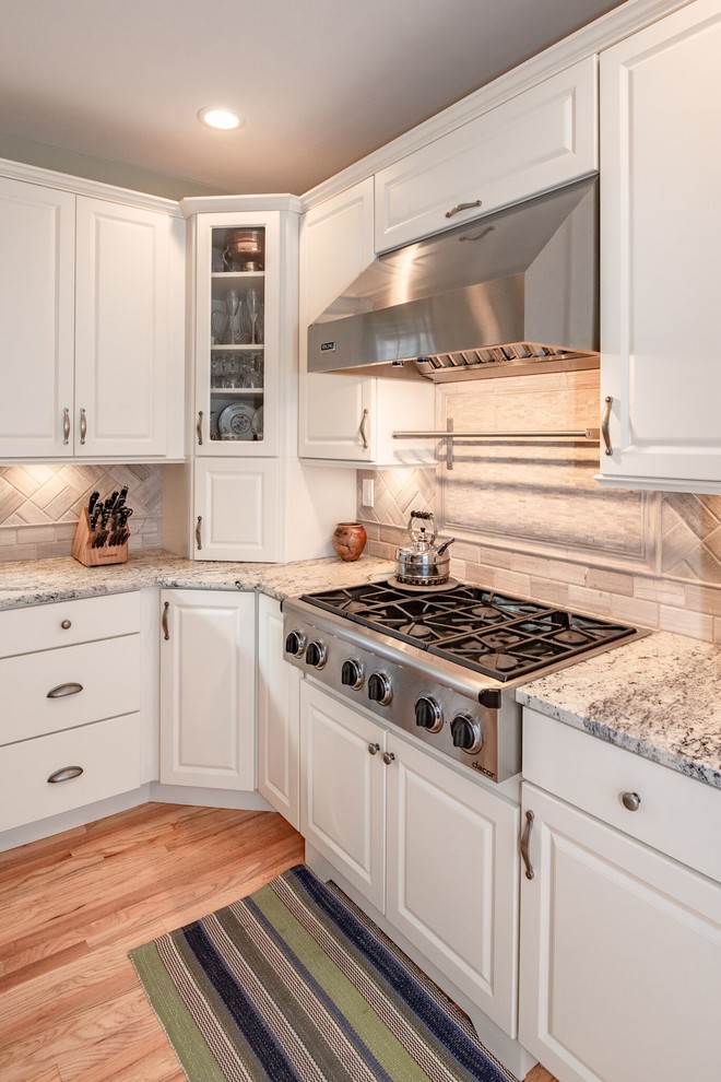 ニューヨークにある広いシャビーシック調のおしゃれなキッチン (ドロップインシンク、レイズドパネル扉のキャビネット、白いキャビネット、クオーツストーンカウンター、グレーのキッチンパネル、セラミックタイルのキッチンパネル、シルバーの調理設備、無垢フローリング、茶色い床、グレーのキッチンカウンター) の写真