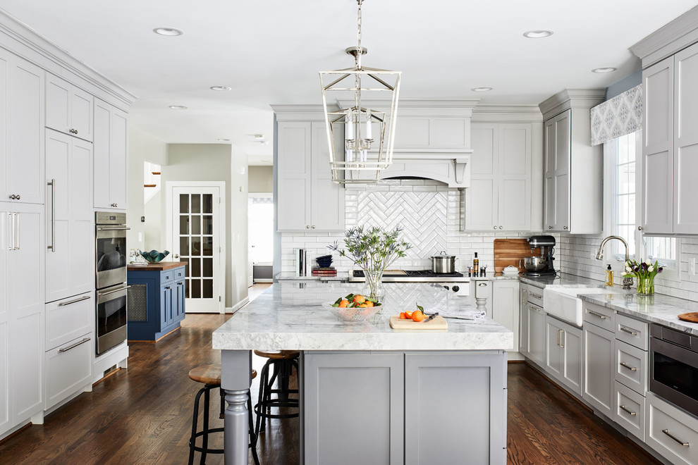 Kitchen - large traditional u-shaped brown floor and dark wood floor kitchen idea in DC Metro with a farmhouse sink, shaker cabinets, gray cabinets, quartzite countertops, porcelain backsplash, stainless steel appliances, an island, gray countertops and white backsplash