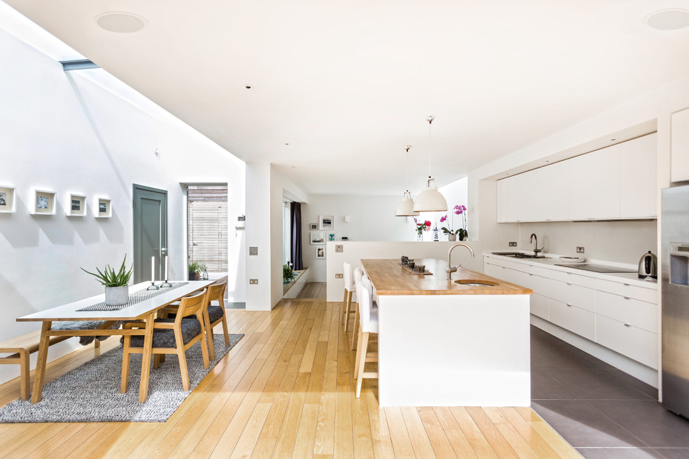 На фото: прямая кухня-гостиная в современном стиле с двойной мойкой, плоскими фасадами, белыми фасадами, столешницей из акрилового камня, серым фартуком и островом с