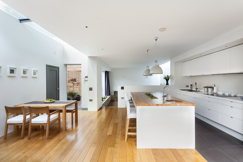 This is an example of a large contemporary single-wall kitchen/diner in London with a single-bowl sink, flat-panel cabinets, white cabinets, an island, grey floors and white worktops.