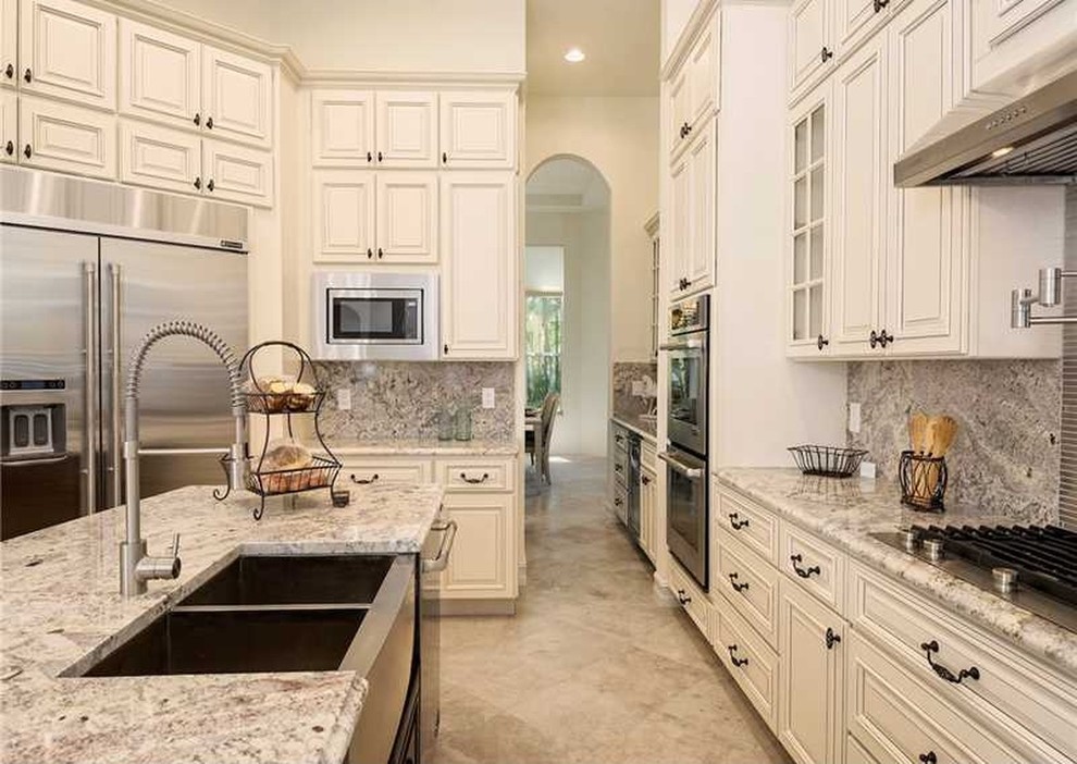 Inspiration for a large mediterranean marble floor eat-in kitchen remodel in Miami with a farmhouse sink, shaker cabinets, beige cabinets, granite countertops, gray backsplash, stone slab backsplash, stainless steel appliances and an island