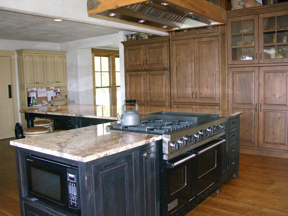 Lantlig inredning av ett mycket stort kök, med en rustik diskho, luckor med profilerade fronter, skåp i mörkt trä, granitbänkskiva, svarta vitvaror, mellanmörkt trägolv och en köksö