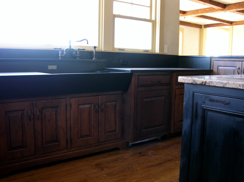 Bild på ett mycket stort lantligt kök, med en rustik diskho, luckor med profilerade fronter, skåp i mörkt trä, granitbänkskiva, svart stänkskydd, stänkskydd i sten, integrerade vitvaror, mellanmörkt trägolv och en köksö