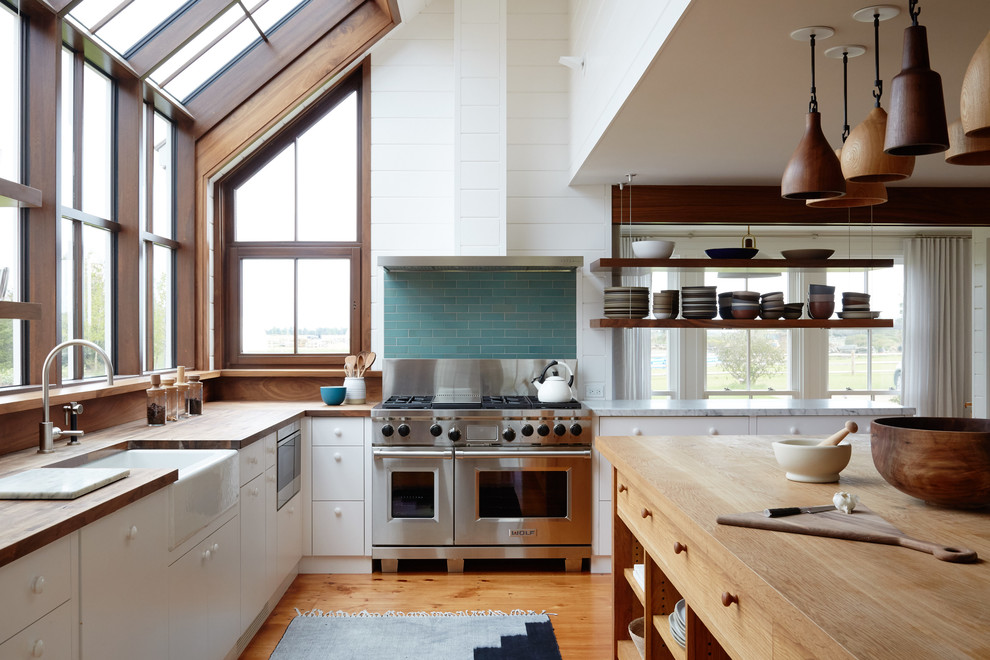 Exempel på ett maritimt l-kök, med en rustik diskho, släta luckor, vita skåp, träbänkskiva, grönt stänkskydd, stänkskydd i tunnelbanekakel, rostfria vitvaror, mellanmörkt trägolv och en köksö