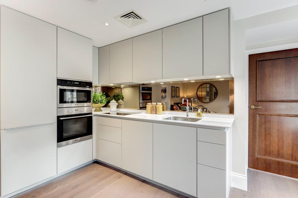 Offene Moderne Küche ohne Insel in L-Form mit Unterbauwaschbecken, flächenbündigen Schrankfronten und Küchengeräten aus Edelstahl in London
