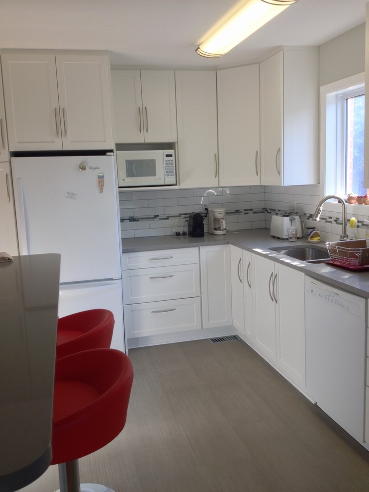 This is an example of a medium sized contemporary l-shaped enclosed kitchen in Ottawa with shaker cabinets, white cabinets, engineered stone countertops, white splashback, metro tiled splashback, white appliances, a double-bowl sink, grey worktops, laminate floors, a breakfast bar and brown floors.