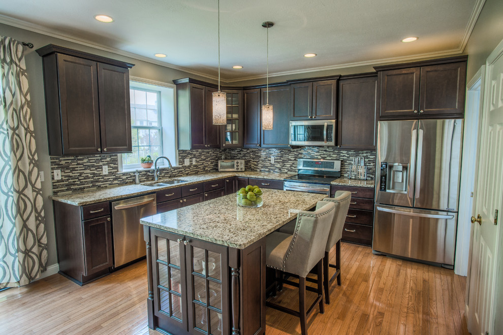 Example of a trendy l-shaped medium tone wood floor eat-in kitchen design in Other with an undermount sink, dark wood cabinets, granite countertops, multicolored backsplash, stainless steel appliances, an island, recessed-panel cabinets and mosaic tile backsplash