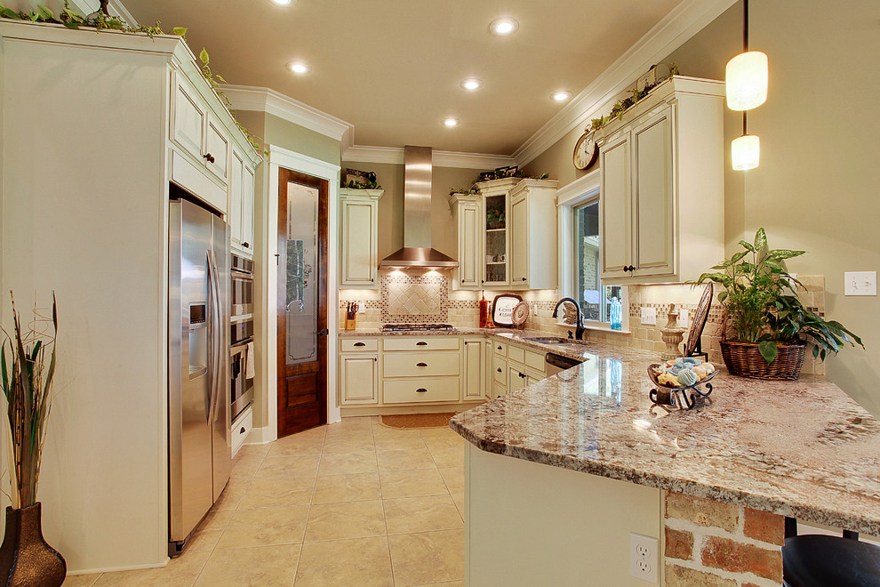 Example of a mid-sized classic porcelain tile kitchen design in New Orleans with an undermount sink, raised-panel cabinets, beige cabinets, granite countertops, beige backsplash, terra-cotta backsplash and stainless steel appliances