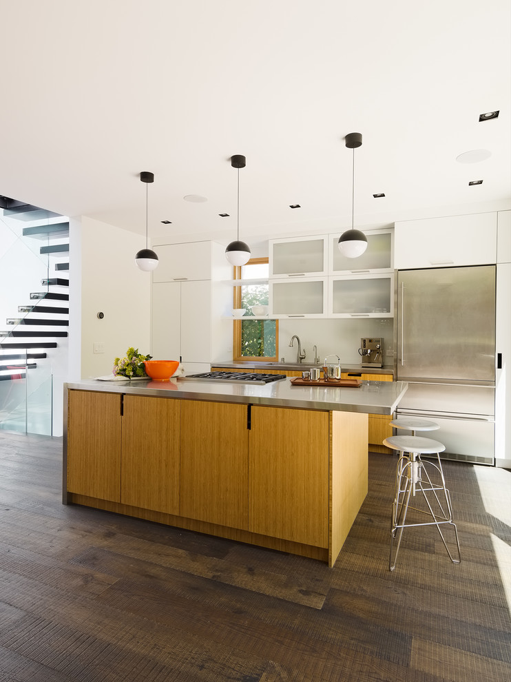 Design ideas for a small contemporary galley open plan kitchen in San Francisco with a single-bowl sink, flat-panel cabinets, light wood cabinets, stainless steel worktops, white splashback, glass sheet splashback, stainless steel appliances, dark hardwood flooring, an island and black floors.