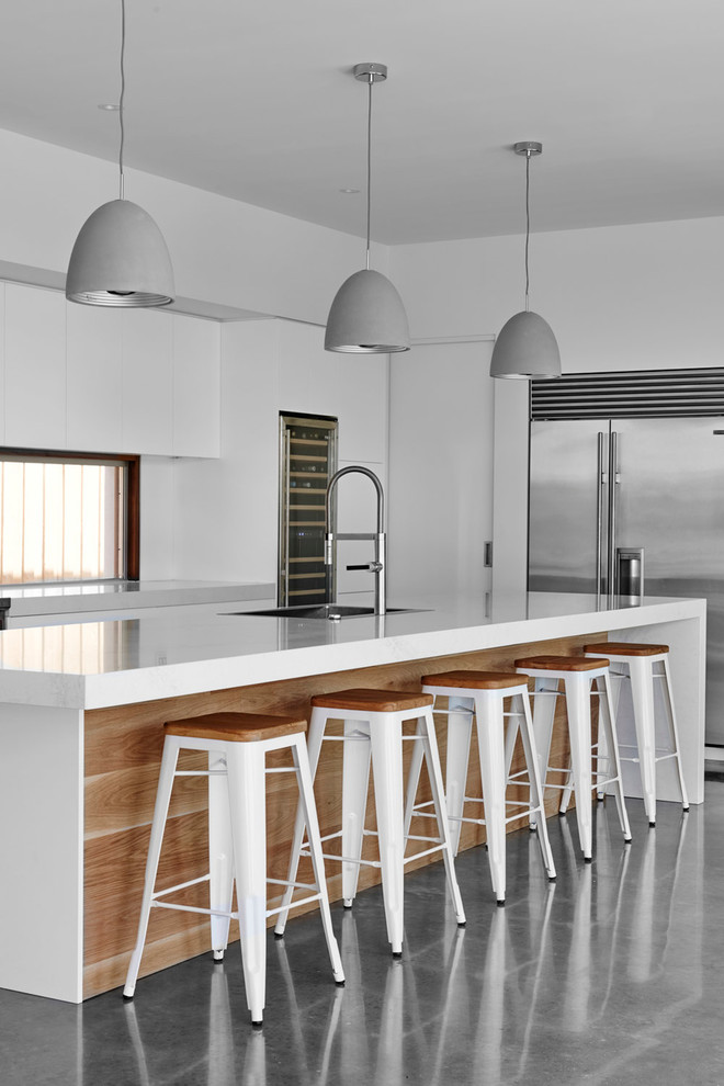На фото: кухня в современном стиле с плоскими фасадами, белыми фасадами, островом и бетонным полом